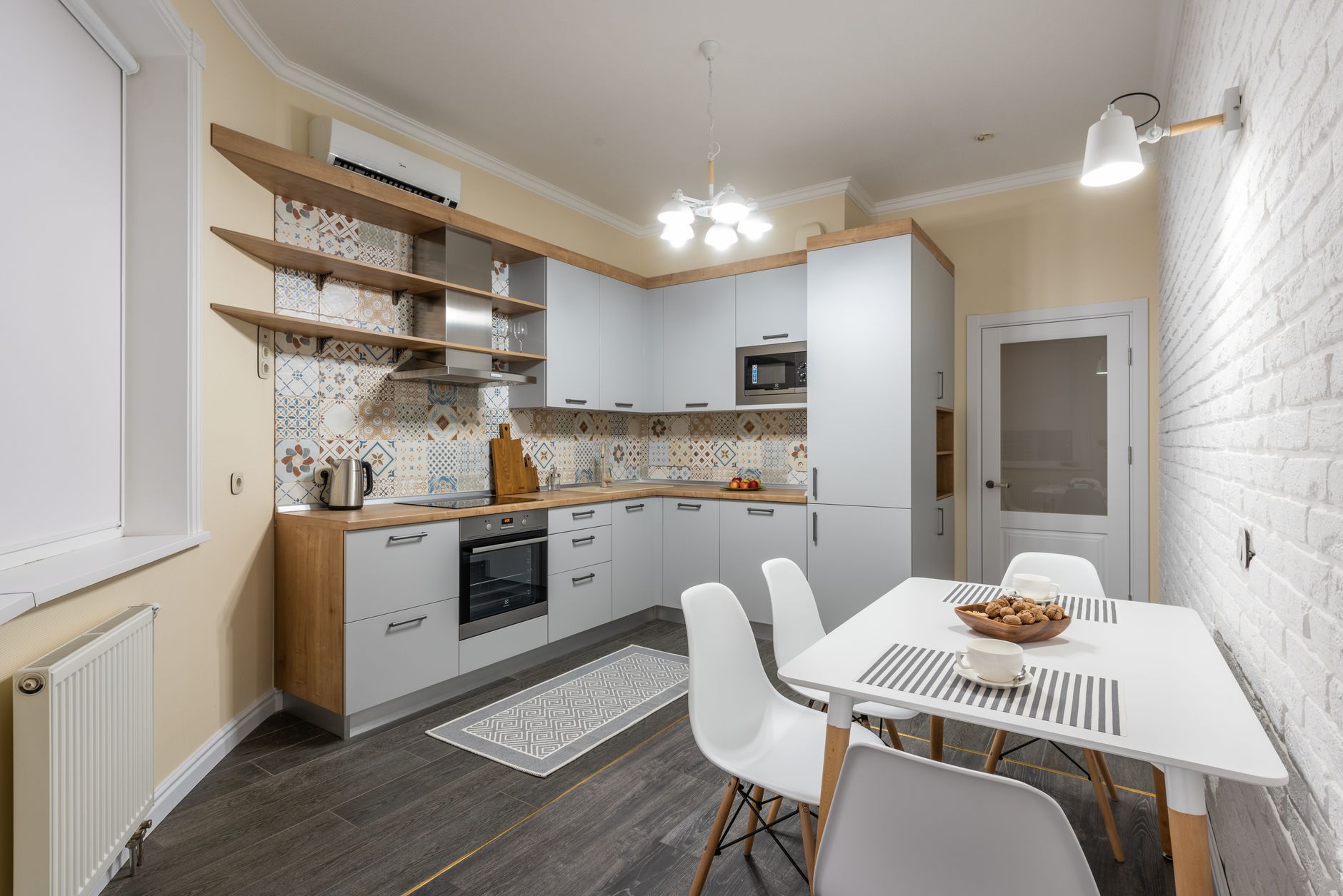 Cuisine moderne avec appareils électriques et radiateur à côté d'une table avec des biscuits savoureux et des tasses illuminées par un lustre lumineux