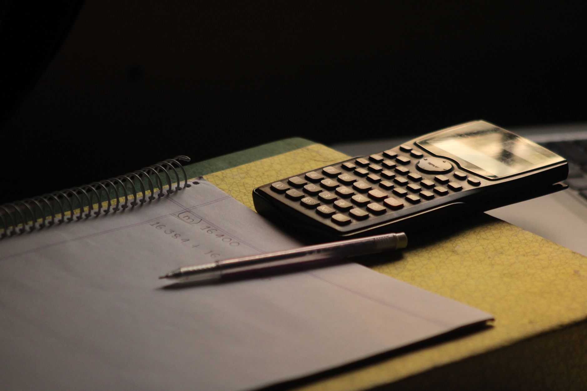 Calculatrice, carnet et stylo posés sur un bureau dans la pénombre